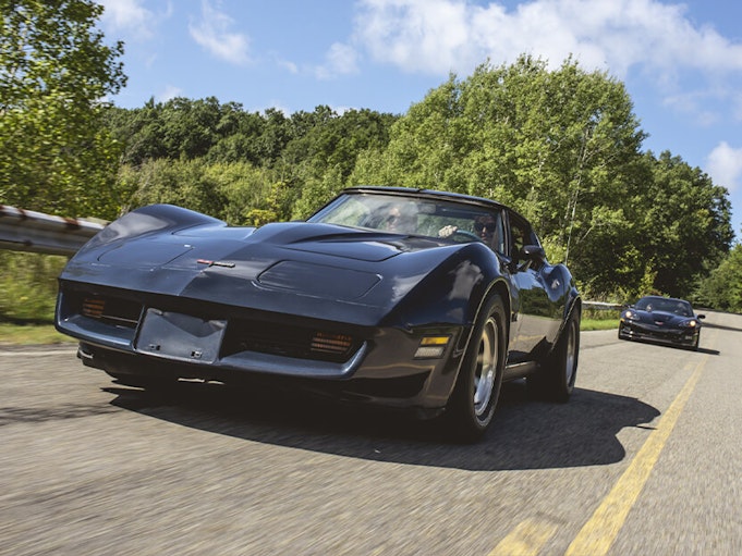 Two collector cars driving fast down a road on a clear day.