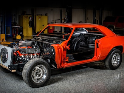 A red collector car without a hood or doors, being restored in a garage