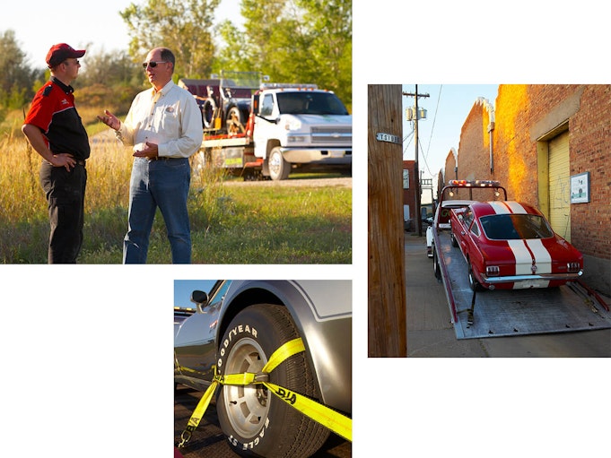 Two men talking next to a white tow truck with a red collector vehicle strapped to it.