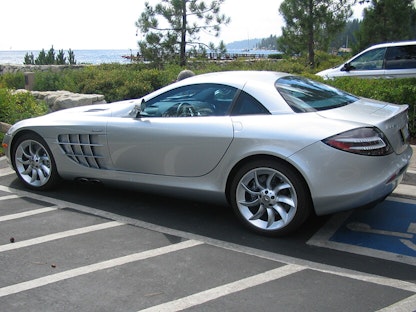 A silver collector car in a parking lot by a beach.