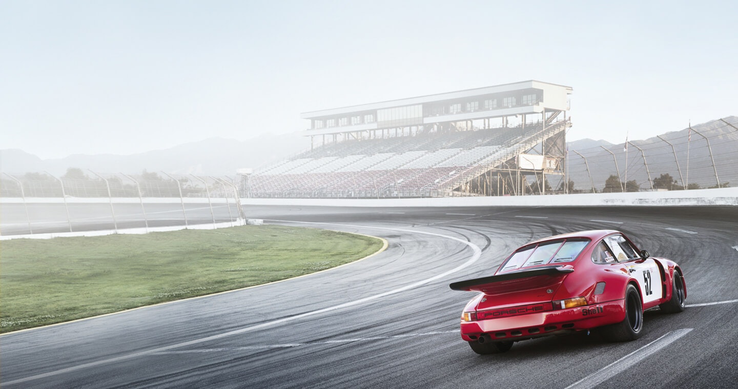 A red collector race car driving solo on a race track, with audience stands in the background.