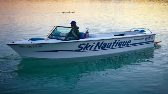 A man on a white boat looking at ducks on a lake.