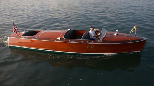 A man directing a red collector boat through still water.